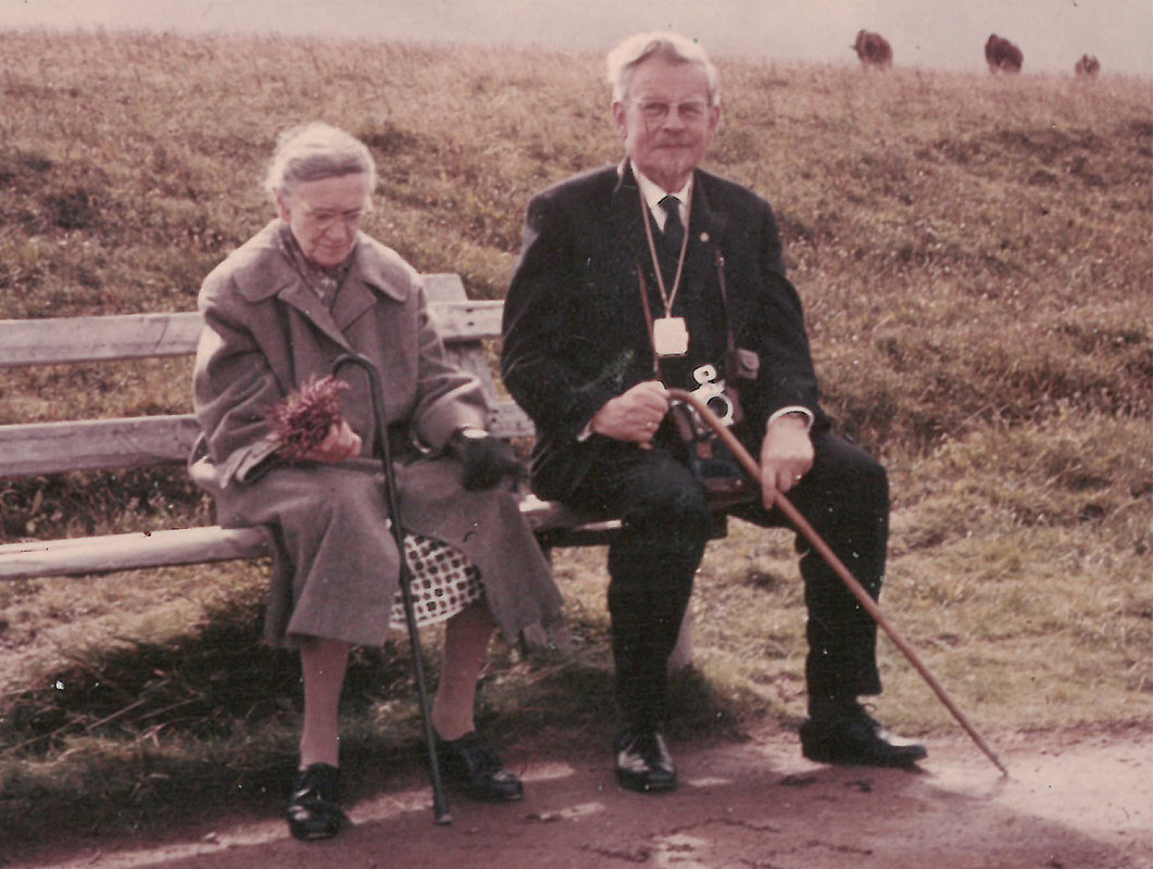 Elisabeth und Wilhelm Jannasch sitzen auf einer Bank, hinter Ihnen ein karges Feld. Beide haben einen Gehstock vor sich.
